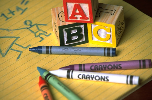 Stock photo of ABC blocks and assorted crayons on a piece of yellow lined paper